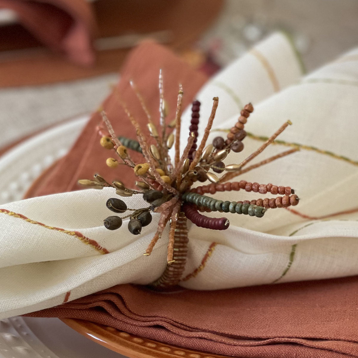 A napkin ring with metal and bead decorations in autumn colors, displayed on a napkin.