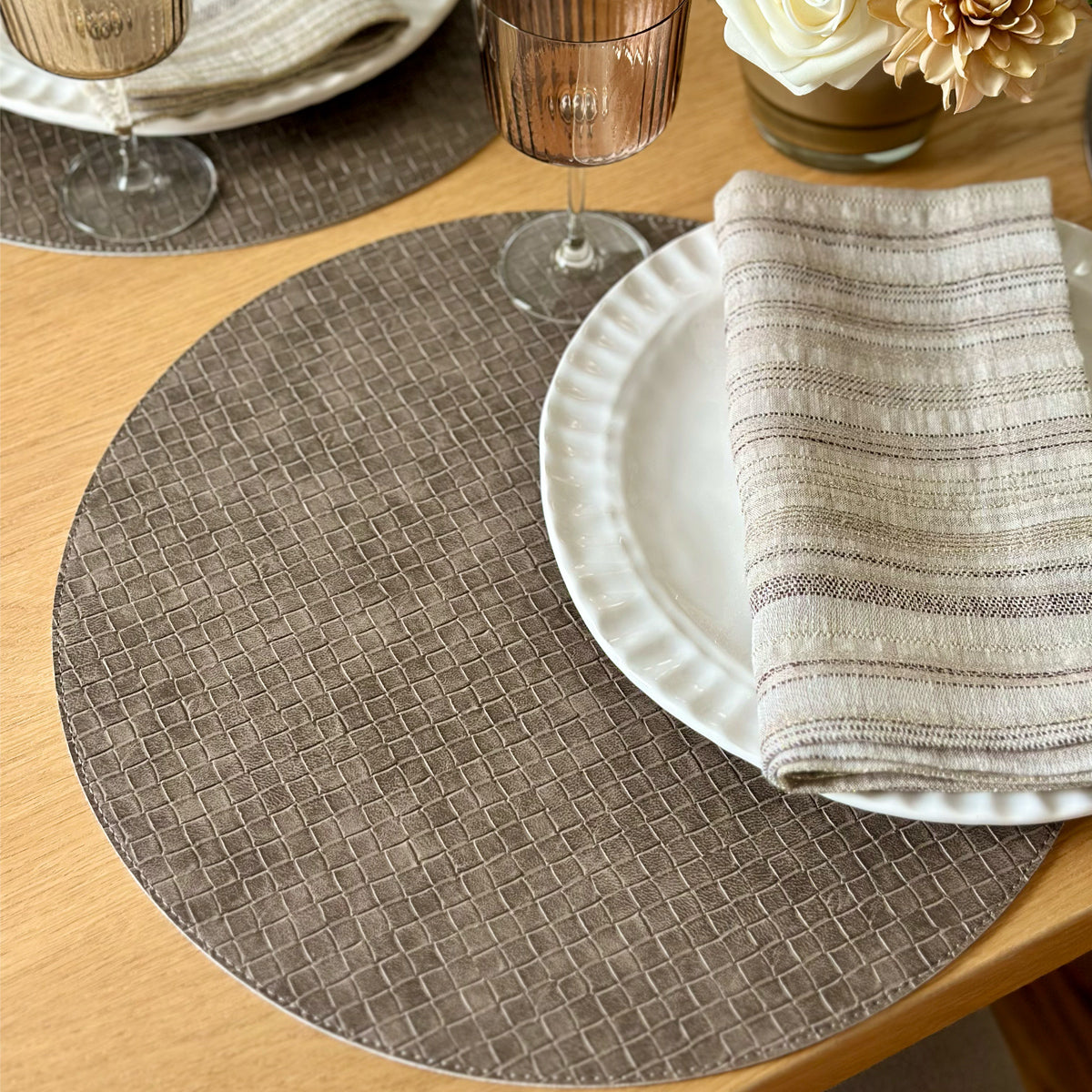 Round woven placemat on a wooden table with a plate and folded napkin.