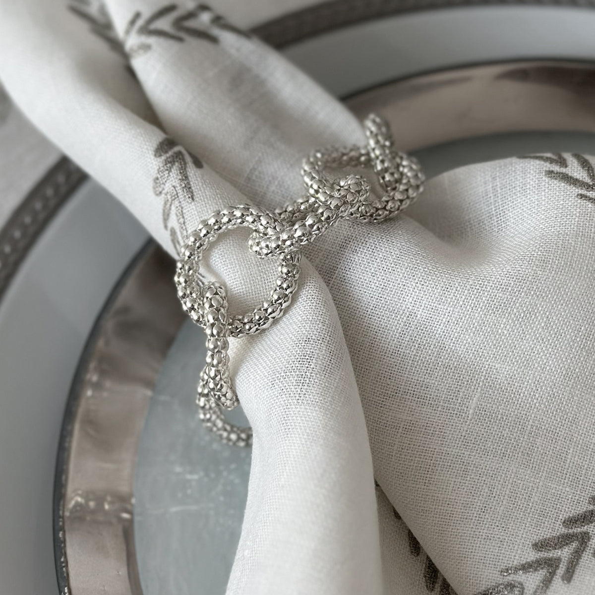 Elegant Chains Silver napkin ring on a white napkins with silver details on top of a silver plate.