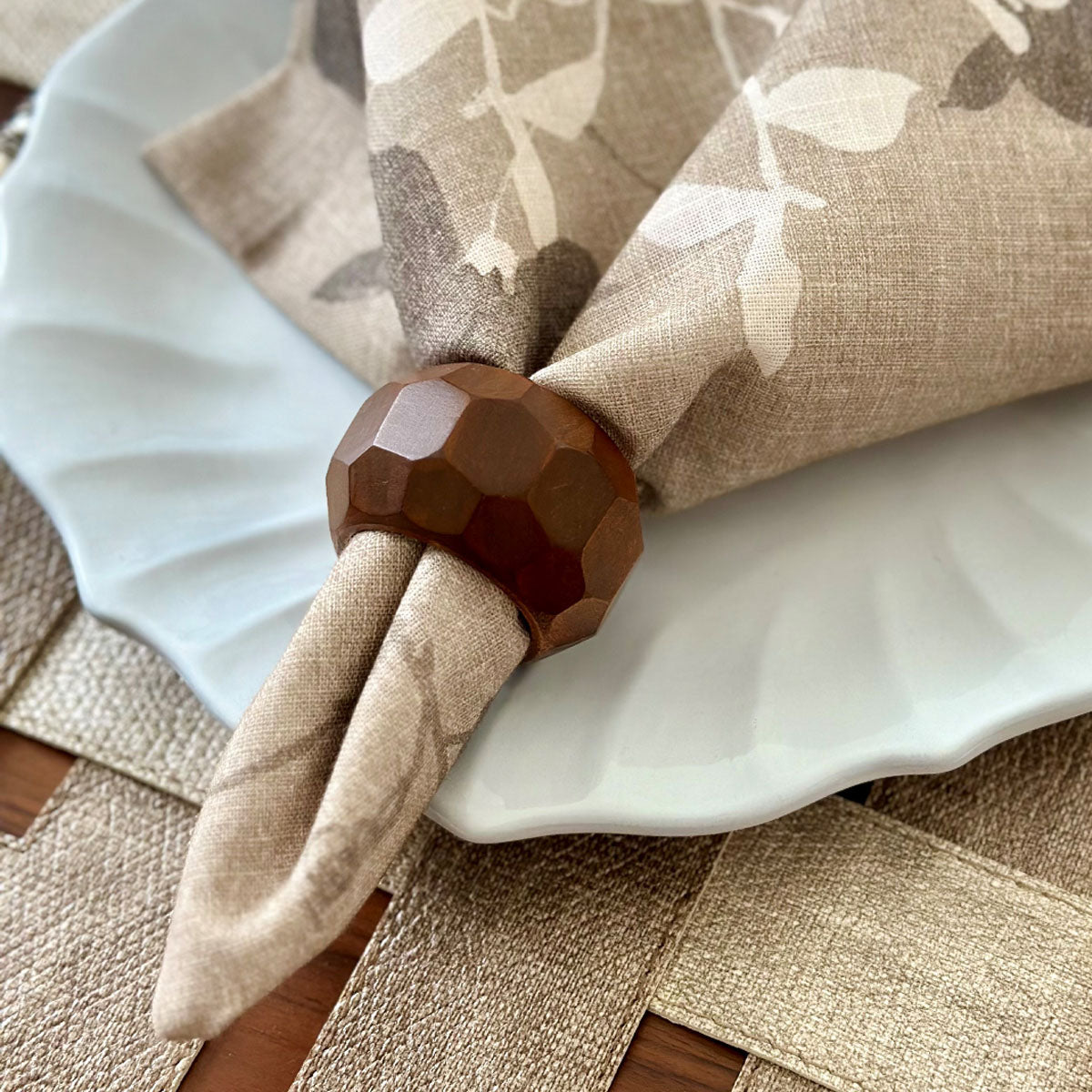 A brown natural wood napkin ring placed on a beige napkin with floral accents over a celtic knot placemat