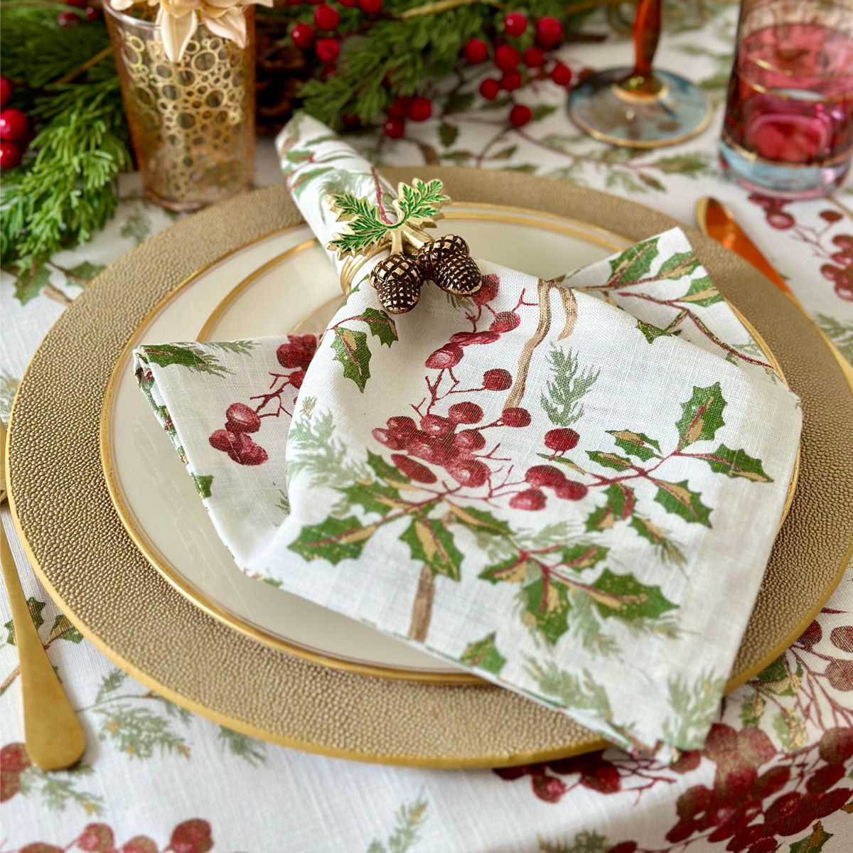 Metallic gold cotton napkin and tablecloth with a print featuring winter berries and leaves, holiday and Christmas setting.