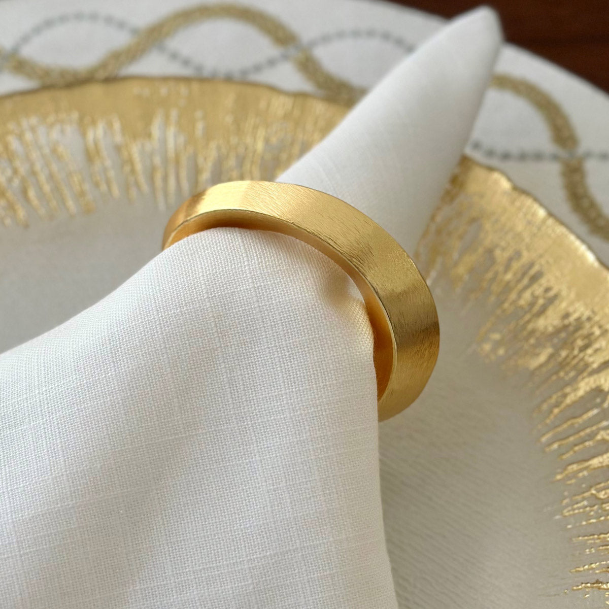 Close up of a gold-colored oval-shaped napkin ring on a white napkin.