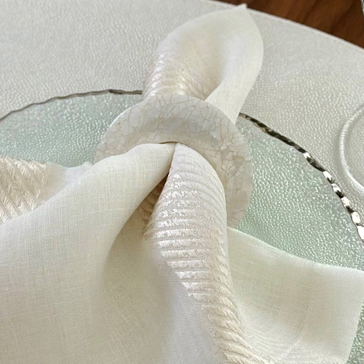 A napkin ring made from mother of pearl shell, displayed on a white napkin.