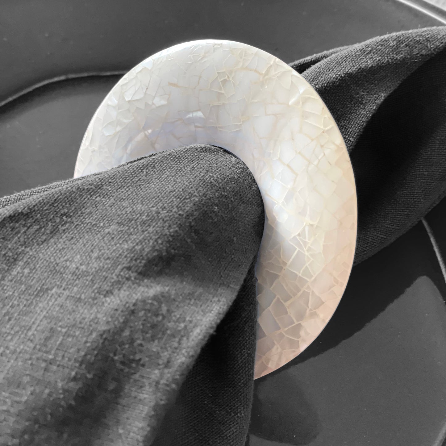 Round napkin ring made out shells on a black napkin. Elegant and refined.