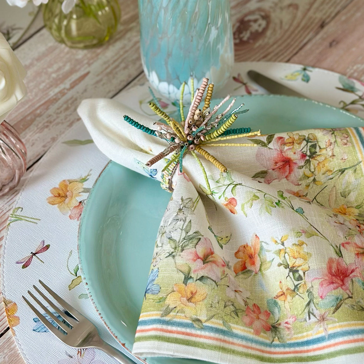 Napkin ring with beads in soft pastel colors on a floral napkin with soft yellow blue orange and green colors