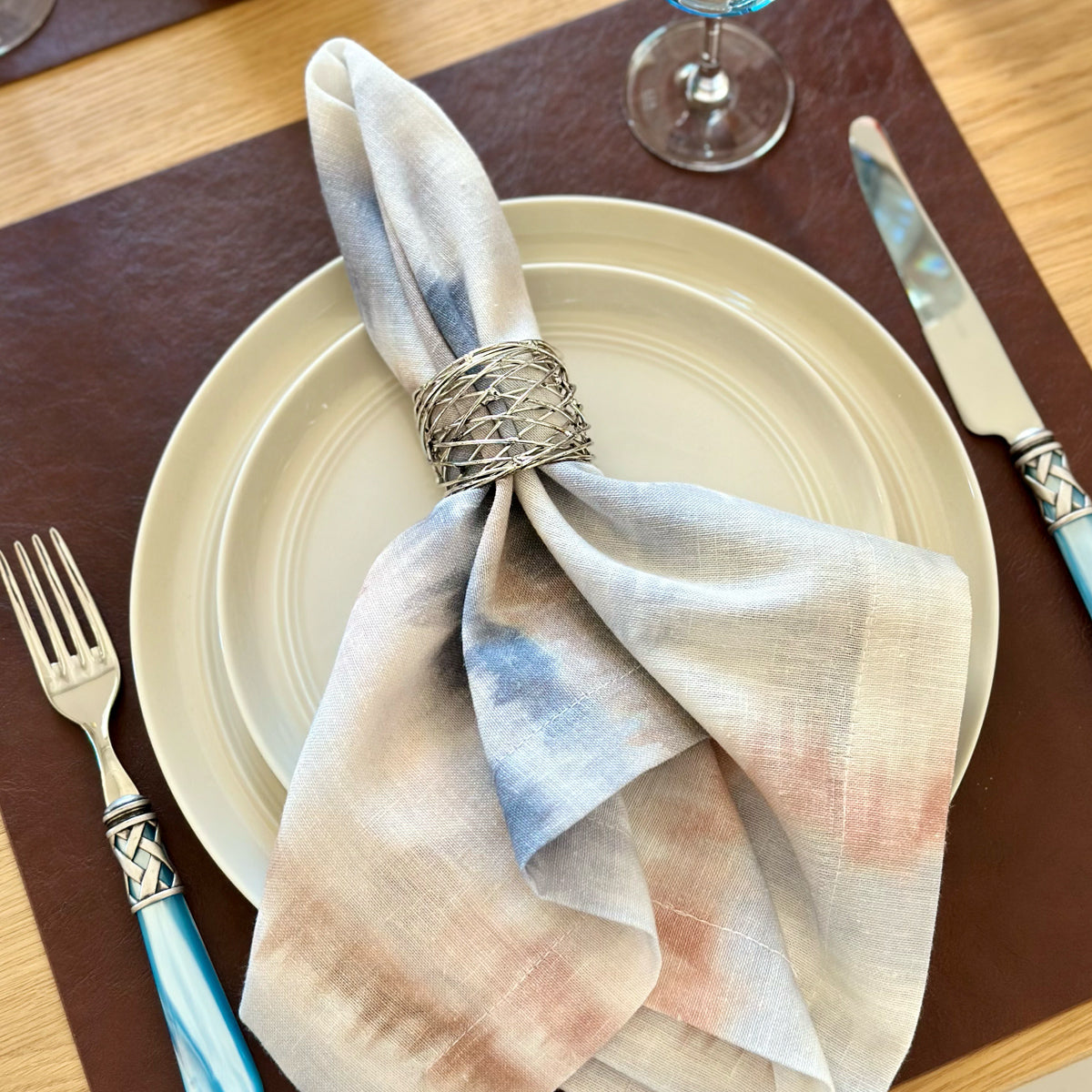 Silver metal napkin ring  used on a tie dye elegant napkin on top of a vegan leather square placemat