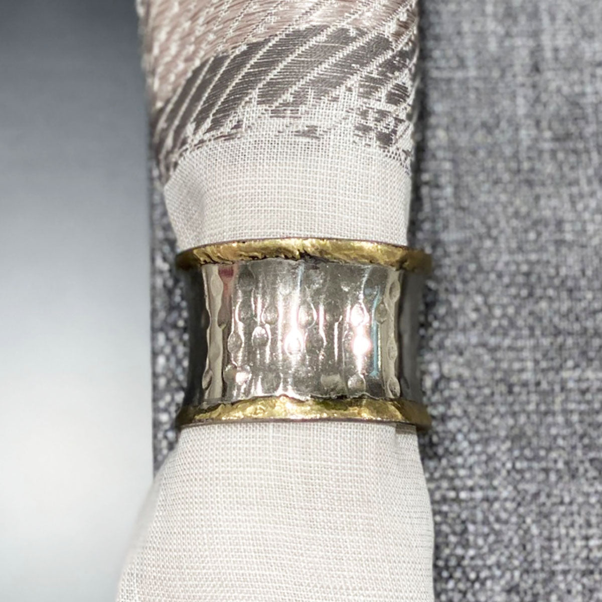 A napkin ring featuring a metallic gold and silver finish, displayed on a napkin with silver accents.