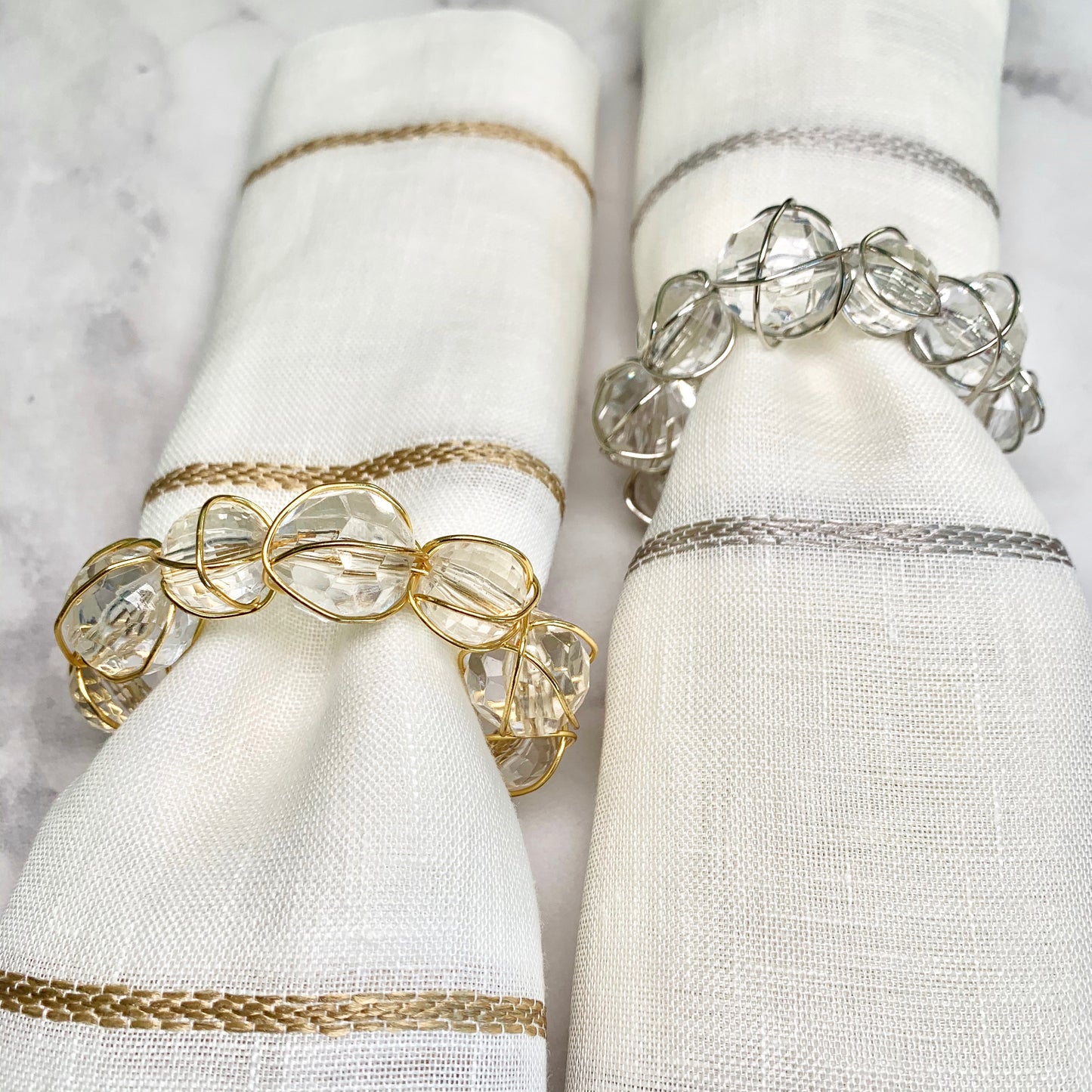 Two clear glass ball napkin rings, one with gold metallic accents and another with silver, displayed on a white napkin.