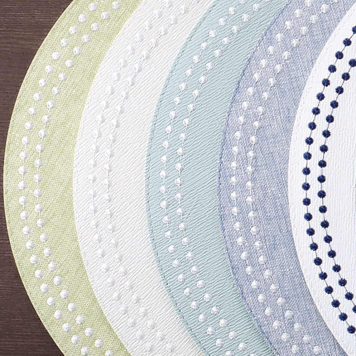 Stacked round vinyl placemats with embroidered dots resembling pearls in a variety of colors. Fern, white, celadon, bluebell and navy.