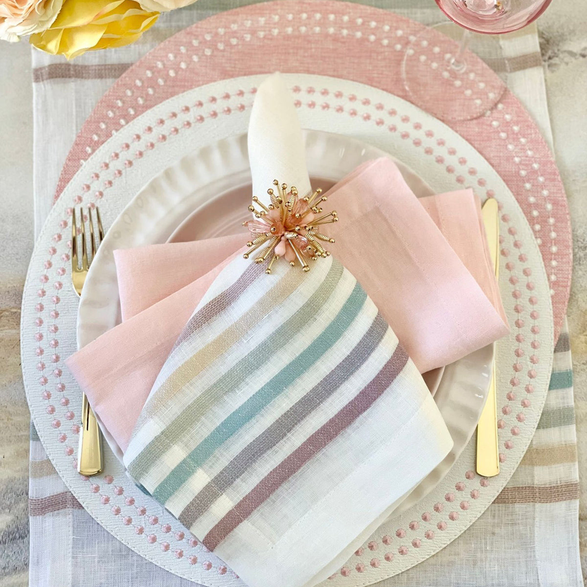 A set of round placemats with pearl-like embroidered dots around the edge, displayed in a home setting with cutlery and a striped napkin. Rose placemats.