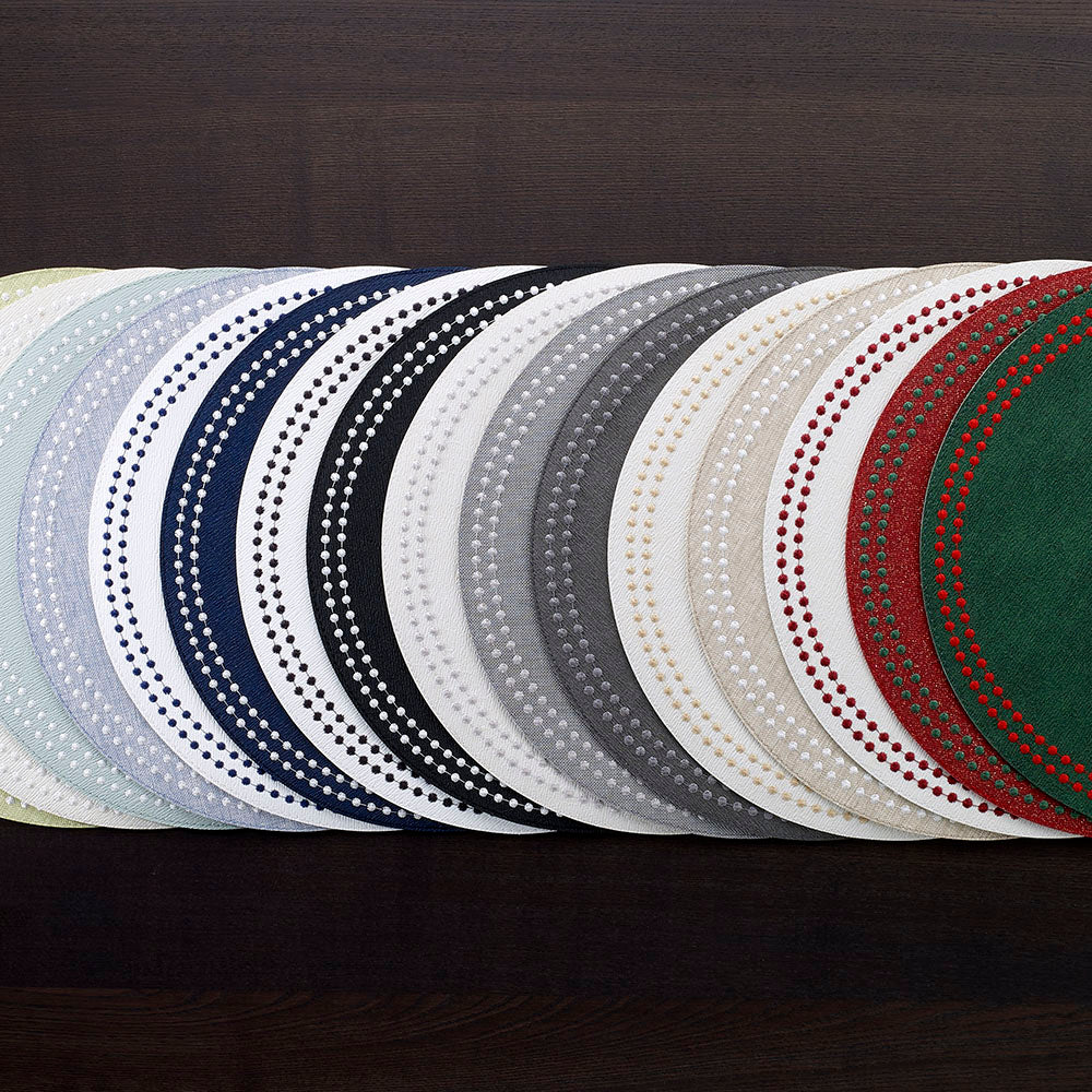 Round vinyl placemats with embroidered pearl details lined up in a variety of colors, gray, black, beige, forest, red, navy, celadon, white.