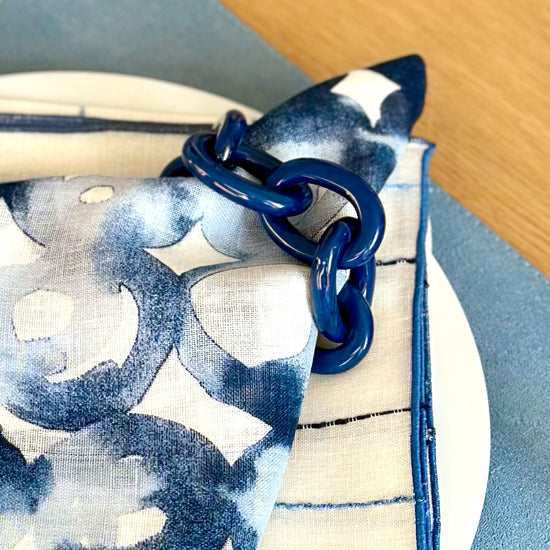Close up of a navy chain link resin napkin ring on a white napkin with watermark design print