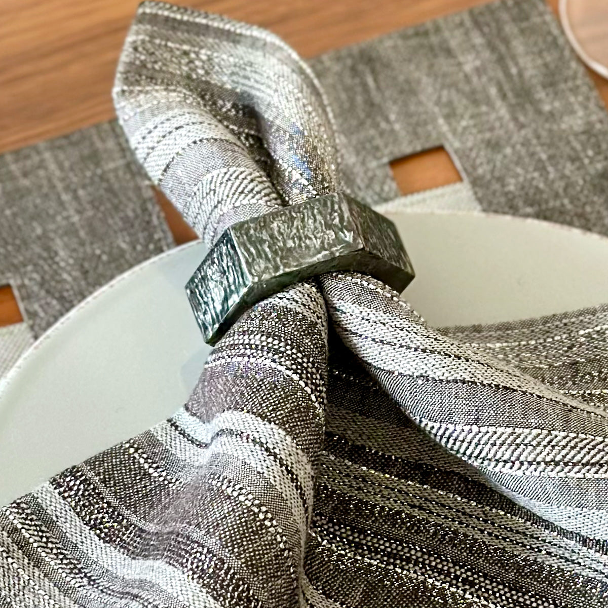 Close up of hexagonal gray resin napkin ring with subtle sparkles to it, on a gray napkin with metallic threads