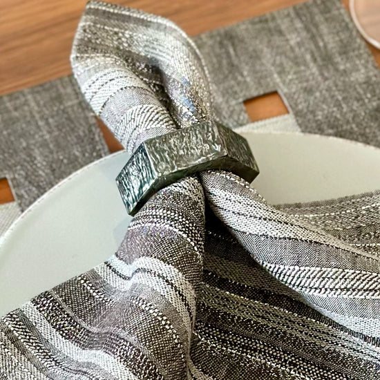 Close up of hexagonal gray resin napkin ring with subtle sparkles to it, on a gray napkin with metallic threads