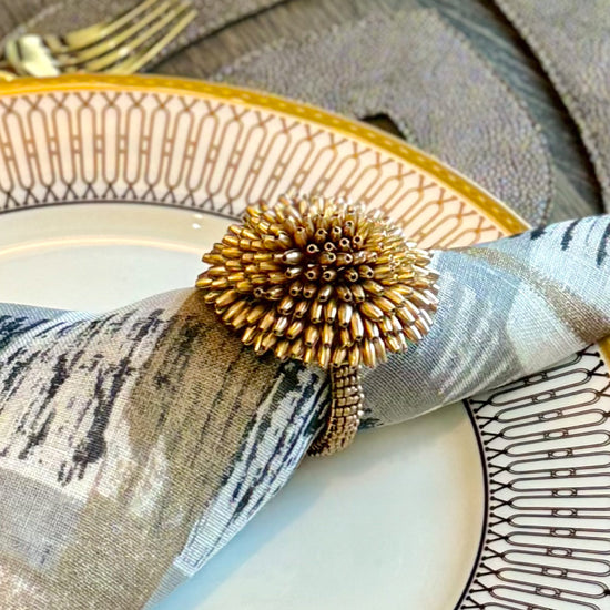 Decorative gold metal napkin ring that looks like a pompom, festive and cheerful
