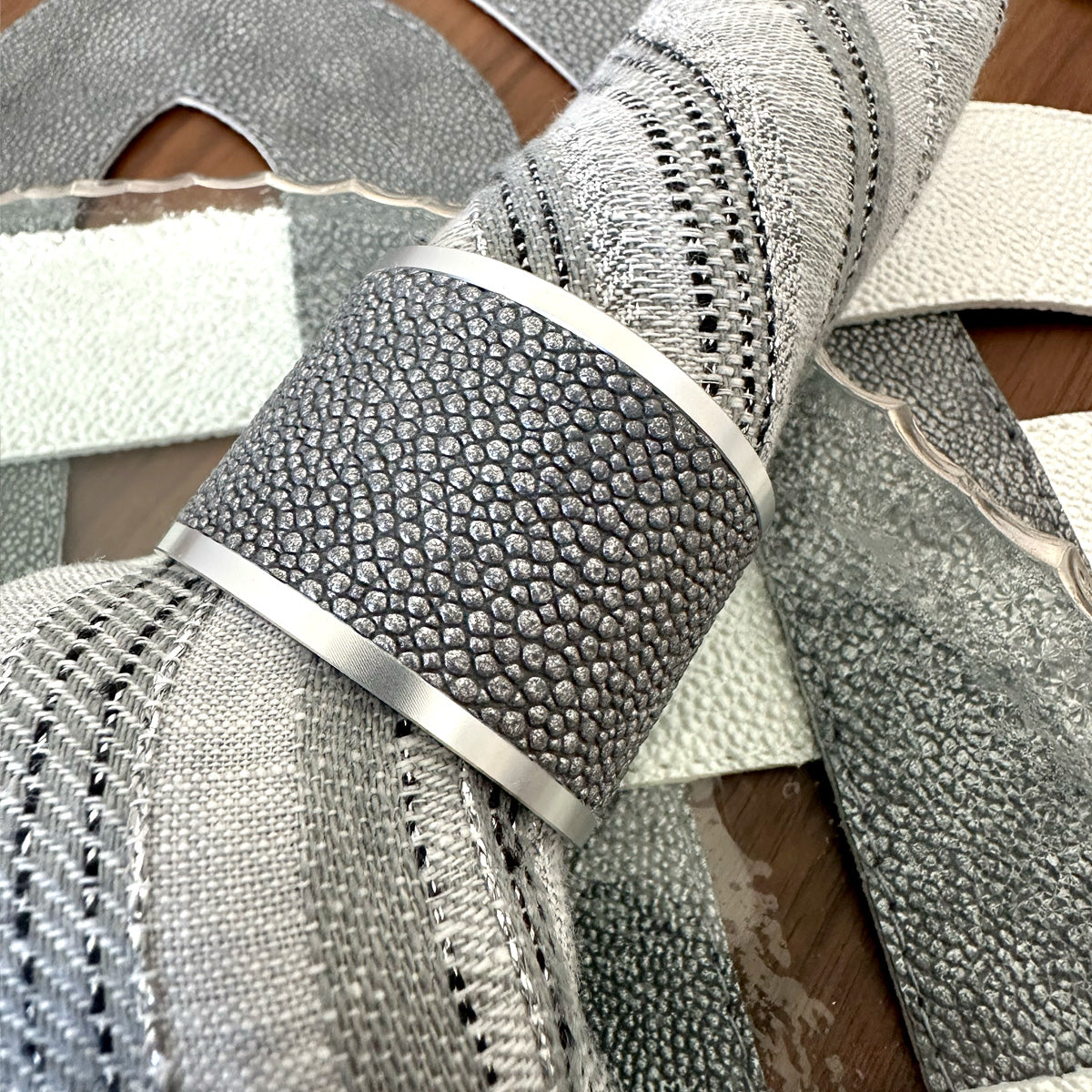 Close up of a gray vinyl napkin ring with metal edges on a gray napkin with metallic threads