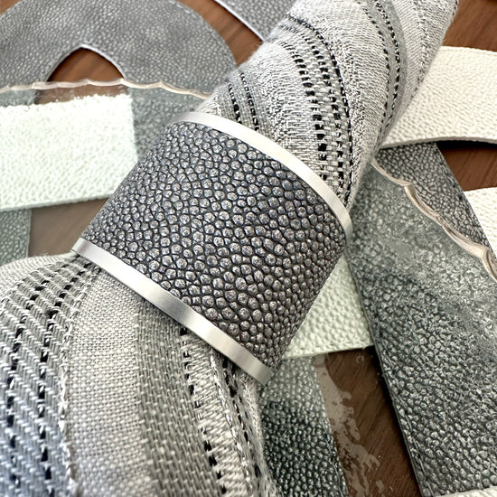 Close up of a gray vinyl napkin ring with metal edges on a gray napkin with metallic threads